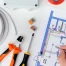 A person reviews an electrical wiring diagram with tools, wire, connectors, and tape arranged on a white surface, preparing for a home remodel.